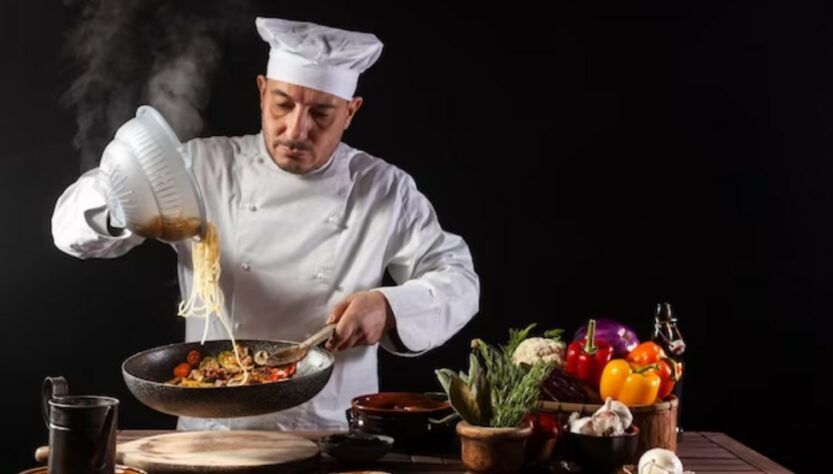 a male chef in white uniform pouring boiled spaghetti into a pan