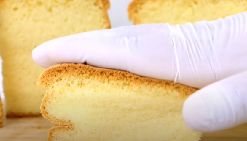 Gloved hand pressing down on a plain sponge cake