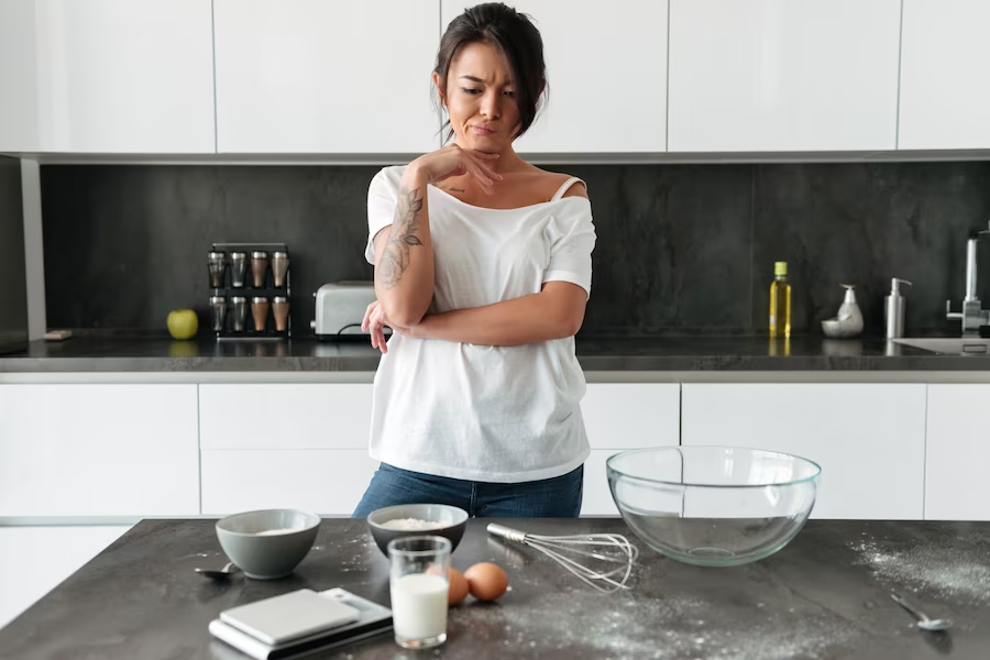 A woman thinking in front of a countertop with various baking ingredients and tools