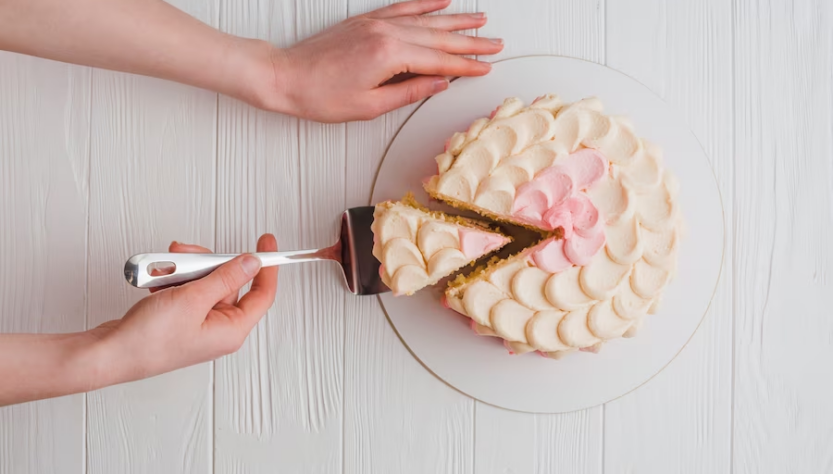 Hand using a cake slicer to cut a slice from a round cake