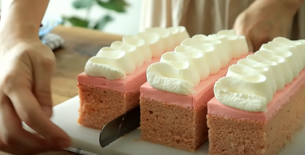Hand slicing rectangular strawberry tres leches cake with whipped cream on top