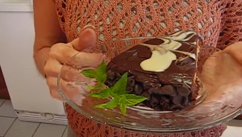 A woman holding a plate with a black tie mousse cake, accompanied by fresh herbs on the side