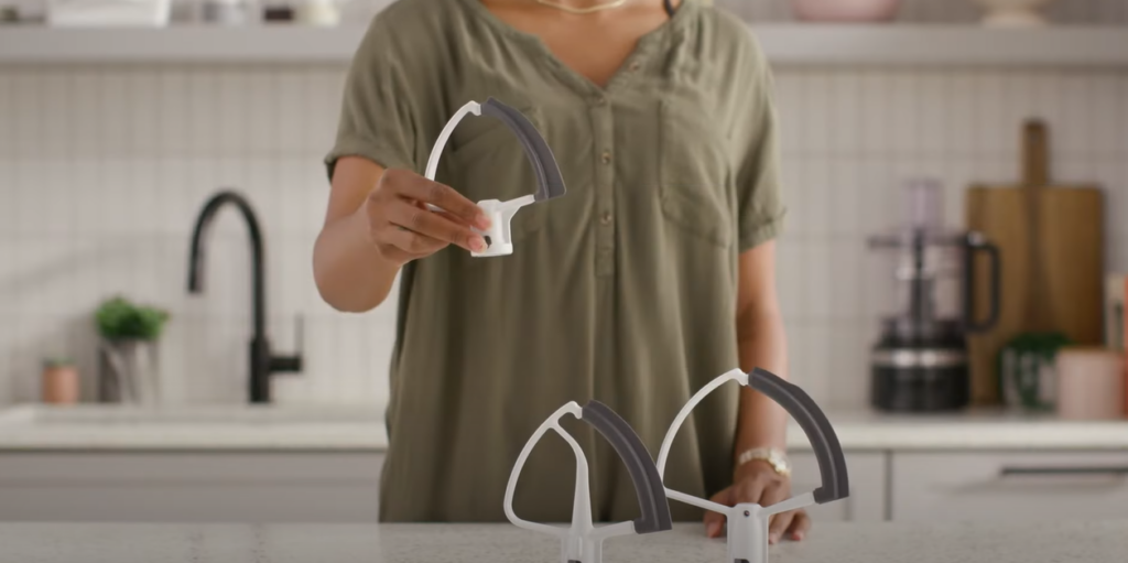 Two KitchenAid Flex Edge Beater Attachments on the table, one being held by a woman's hand
